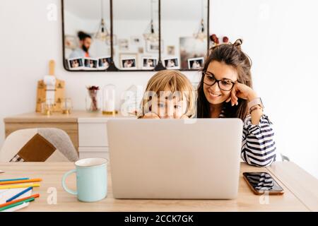 Madre sorridente con figlia che usa un computer portatile sul tavolo da pranzo casa Foto Stock