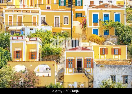 SYMI, Grecia - 27 giugno 2019: Vista dei luminosi edifici di colore giallo con porte e finestre multicolore nella città di Symi allacciata su una costa di Symi isla Foto Stock