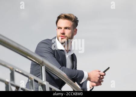 In attesa chiamata importante dal partner. Imprenditore utilizza lo smartphone per le video chiamate o messaggi di testo sullo sfondo del cielo. Uomo in tuta imprenditore assume i vantaggi delle moderne tecnologie mobili per il business. Foto Stock