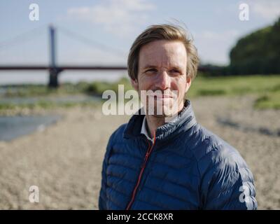 Primo piano di un uomo sorridente pensieroso che guarda lontano mentre si sta in piedi terra Foto Stock