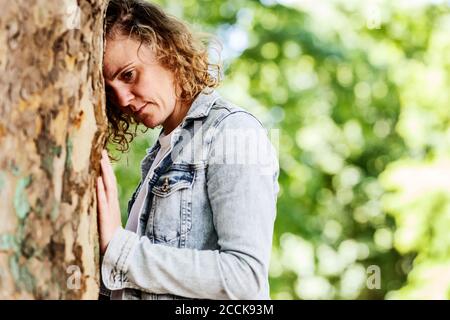 Primo piano di donna pensierosa appoggiata sul tronco dell'albero nel parco Foto Stock