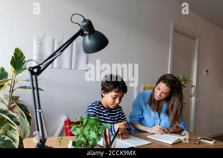 Sorridente tutor femminile che guarda il ragazzo che studia sul tavolo Foto Stock