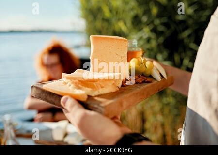 Uomo che serve un piatto di formaggi per gli amici in un lago Foto Stock