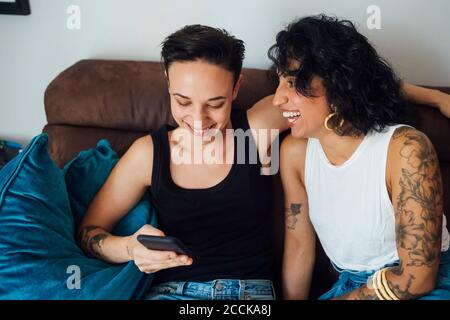 Donna allegra che guarda il compagno usando il telefono sul divano Foto Stock