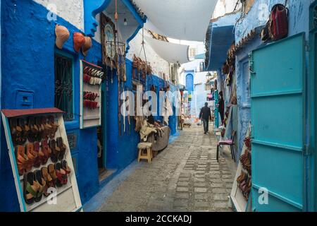 Vari articoli in vendita appesi alla parete blu a vicolo, Chefchaouen, Marocco Foto Stock