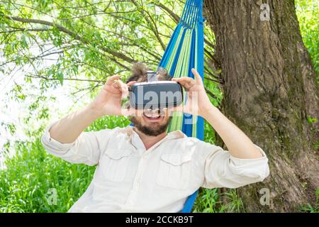 Uomo con occhiali 3d che si rilassa sull'amaca sul lungofiume Foto Stock