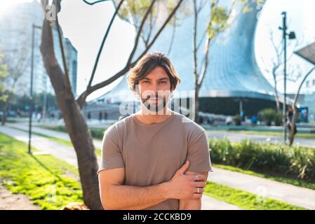 Uomo bearded in piedi sulla strada contro l'edificio moderno mentre si è in viaggio in città Foto Stock