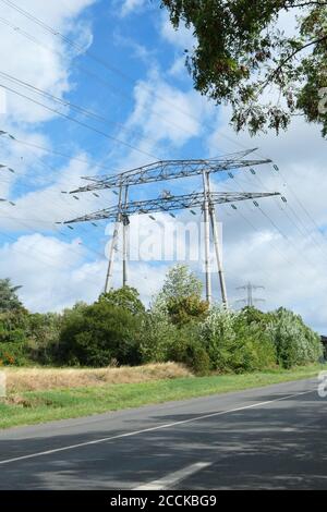 Gruppo di tralicci elettrici, linee ad alta tensione. Cavi sospesi che trasportano l'elettricità alle città. Strada in primo piano. Foto Stock