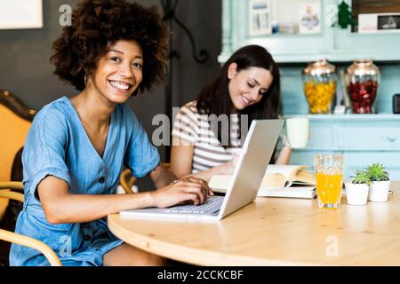 Felici le amiche che studiano con il computer portatile nel bar Foto Stock