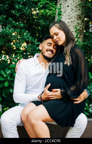 Donna incinta seduta sul grembo di un uomo sorridente nel parco Foto Stock