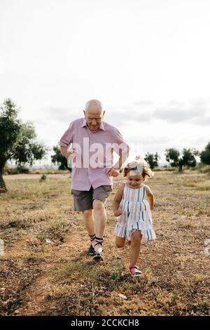 Nonno giocoso con la nipote che corre sulla terra contro il cielo Foto Stock