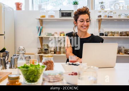 Donna sorridente che usa il computer portatile sull'isola della cucina alla scuola di cucina Foto Stock