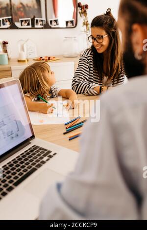 Padre che lavora su un computer portatile mentre madre e figlia parlano sala da pranzo Foto Stock