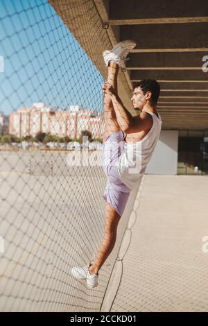Giovane uomo che fa ginnastica ritmica con recinzione chainlink Foto Stock