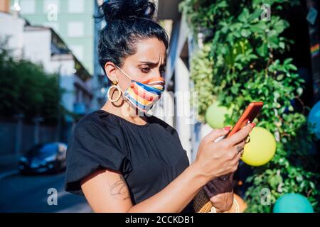 Donna preoccupata che usa il telefono mentre indossa la maschera in città Foto Stock