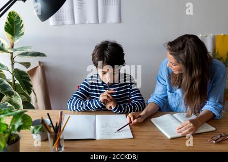 Tutor femminile che spiega al ragazzo attraverso il libro sul tavolo a. casa Foto Stock