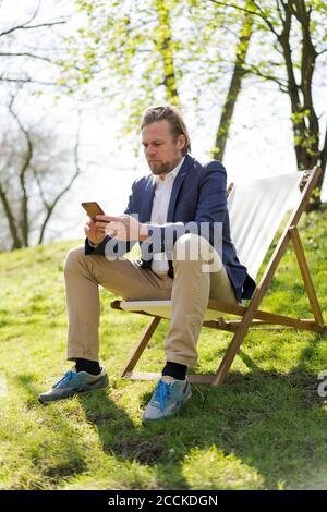 Messaggi di testo per uomini d'affari maturi tramite telefono cellulare mentre ci si siede sedia al parco Foto Stock