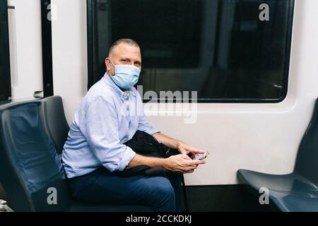 Uomo d'affari che indossa la maschera mentre si viaggia in treno della metropolitana durante COVID-19 Foto Stock