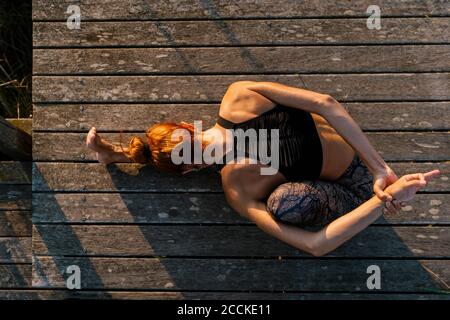 Giovane atleta che allunga il corpo mentre si siede sul molo Foto Stock