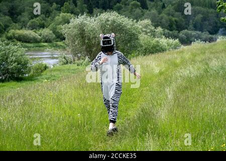 Ragazzo che indossa un costume zebra utilizzando un simulatore VR mentre cammina erba Foto Stock