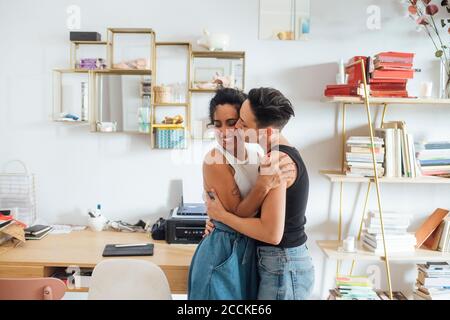 Giovane donna baciando sorridente partner in soggiorno Foto Stock