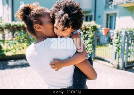 Madre che porta la figlia felice mentre si trova sul sentiero durante il sole giorno Foto Stock