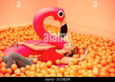 Giovane donna allegra con fenicottero gonfiabile sdraiato in palla arancione buca Foto Stock