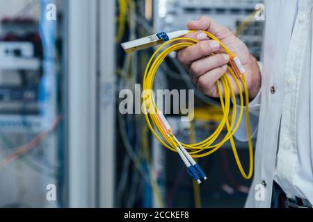 Primo piano di un uomo maturo che tiene i cavi gialli nel data center Foto Stock