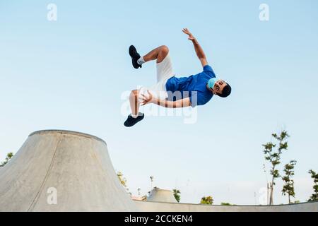 Giovane uomo che indossa la maschera facendo il sideflip contro il cielo limpido Foto Stock