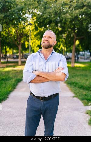 Uomo d'affari sorridente in piedi con le braccia incrociate al parco ufficio Foto Stock