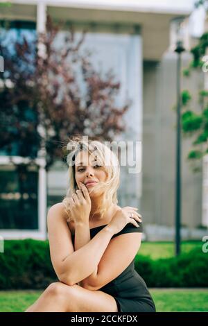 Giovane donna che indossa un abito nero seduto al parco in città Foto Stock