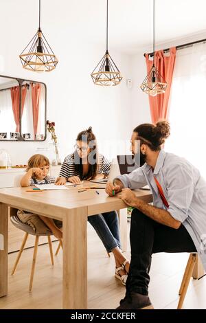 I genitori che guardano la pittura carina della figlia sul tavolo da pranzo a. casa Foto Stock