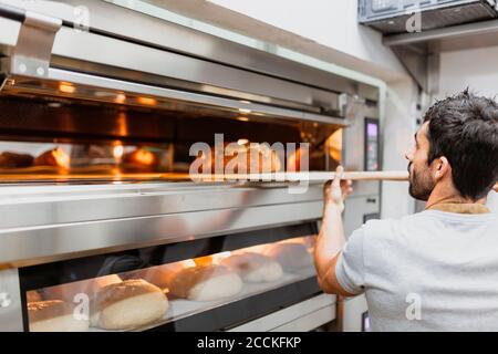 Panettiere che cuoce il pane nel forno al forno Foto Stock