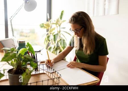 Donna d'affari che scrive sulla carta mentre sedendo nell'ufficio domestico Foto Stock