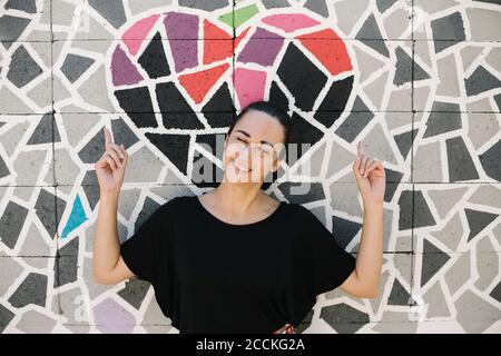 Ritratto di donna sorridente che mostra sul cuore su una parete colorata mosaico Foto Stock