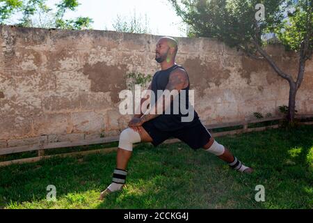 Uomo maturo calvo che si esercita su terra erbosa contro muro in iarda Foto Stock