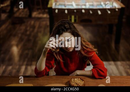 Triste donna che tiene il bicchiere di birra mentre si siede al tavolo ristorante Foto Stock