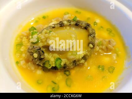un abalone brasato in salsa gialla in recipiente bianco Foto Stock