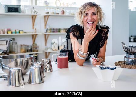 Donna che mangia frutta mentre si appoggia sull'isola della cucina a cucinare scuola Foto Stock