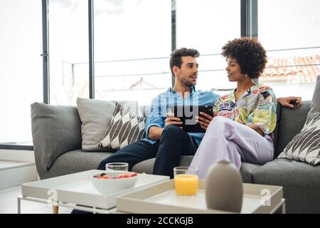 Una coppia multietnica che utilizza un tablet digitale mentre si è seduti sul divano attico moderno Foto Stock