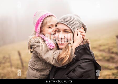Madre e figlia abbracciano e ridono in un paesaggio foggoso Foto Stock