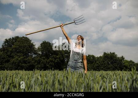 Urlando giovane donna che solleva la forchetta di fieno in un grano campo in campagna Foto Stock