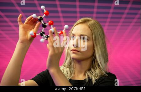Primo piano di una scienziata femminile che tiene il modello di molecola contro il modello di griglia Foto Stock