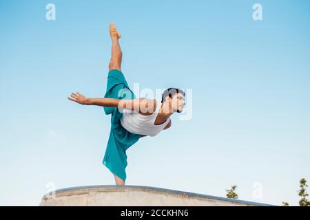Giovane uomo che fa ginnastica ritmica contro il cielo blu chiaro Foto Stock