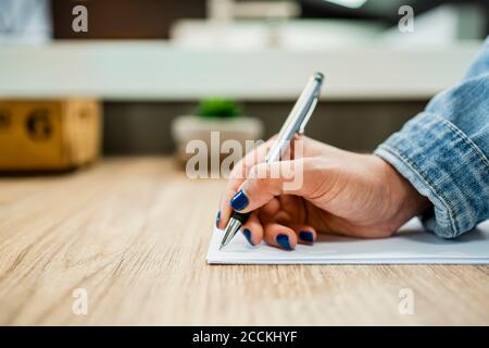 La mano di una donna d'affari scrive su un documento alla scrivania in legno in stile moderno ufficio Foto Stock