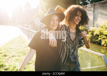 Uomo allegro che tiene la chitarra con la mano sulla spalla della ragazza che cammina nel parco durante la giornata di sole Foto Stock