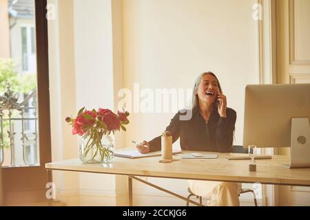 Donna d'affari matura che parla al telefono mentre lavora a casa Foto Stock