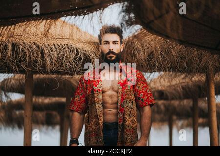 Attraente uomo bearded con camicia colorata in piedi tra ombrelloni da spiaggia Foto Stock