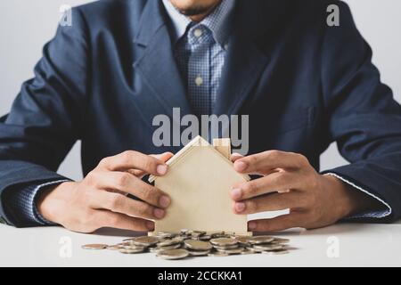 Mano di uomo di affari che tiene moneta messo in banca piggy con pila di denaro crescente crescita risparmio di denaro, concetto di investimento per il commercio di libertà finanziaria. Foto Stock