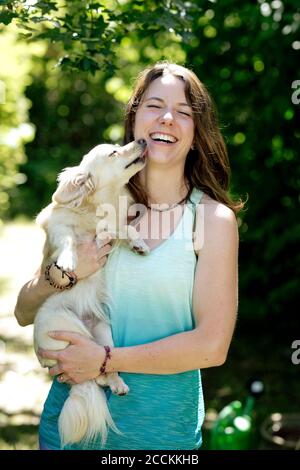 Giovane donna allegra che porta un cane giocoso leccando la faccia dentro foresta Foto Stock